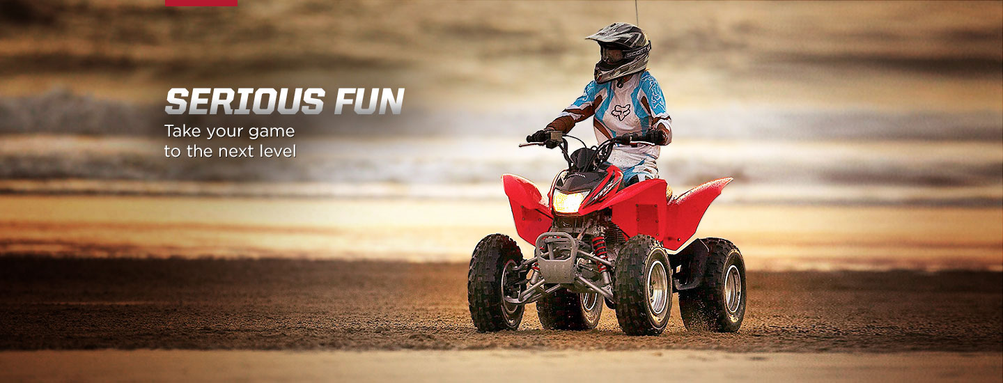 Serious Fun. Take your game to the next level. Image of determined rider in ATV sport suit riding red ATV on rocky incline.