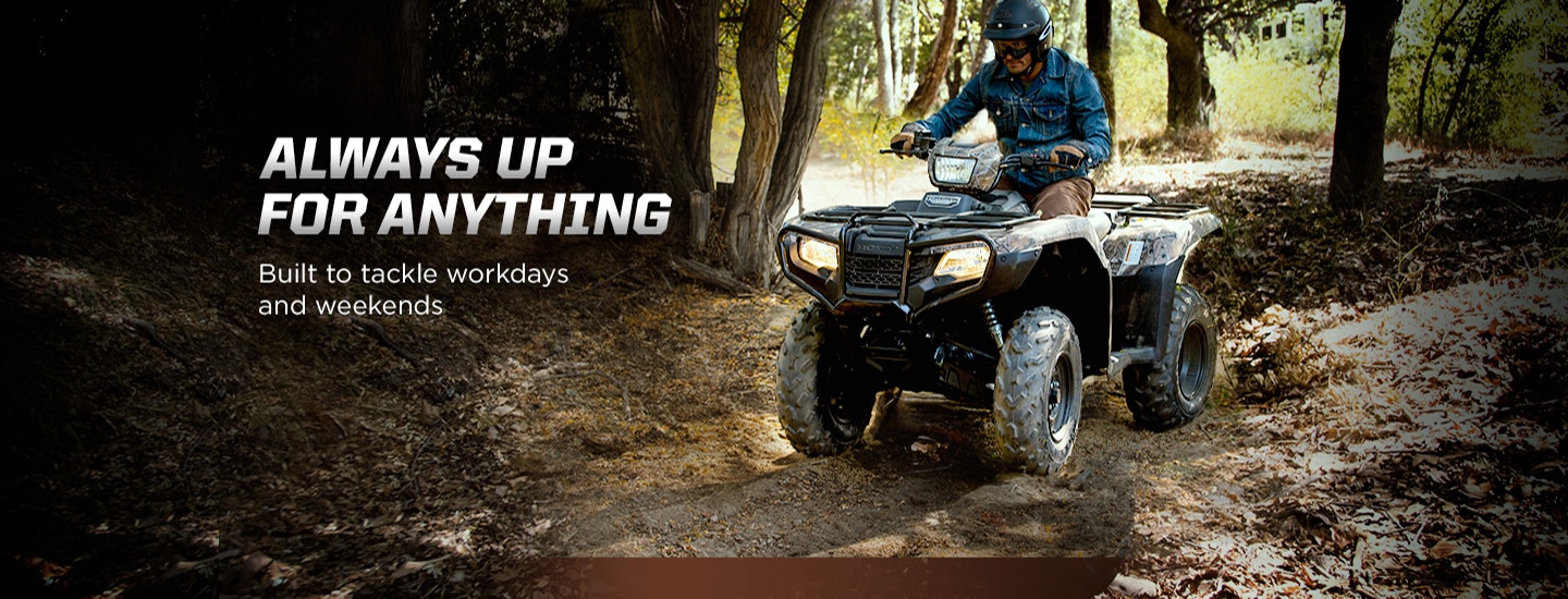 Always up for anything. Built to tackle workdays and weekends. Image of man in denim shirt riding black ATV on muddy forest trail.